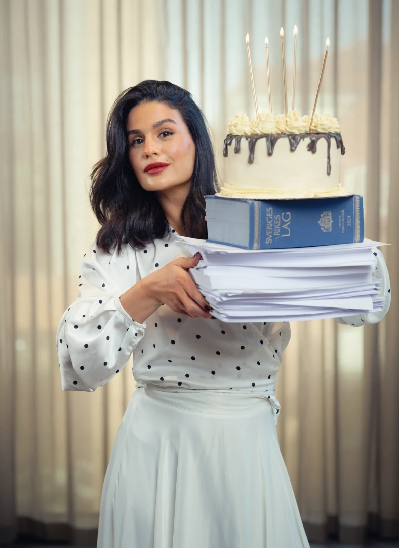 Lasia – Arbetsrätt för alla. Kvinna som håller i en bunt med papper. På papperna ligger Sveriges lagbok och där på står en tårta.