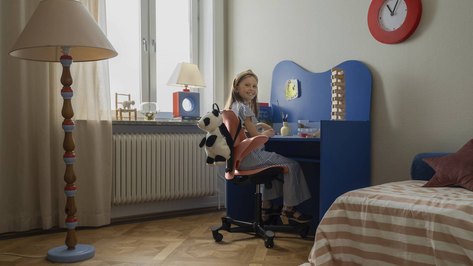  Young girl sits at her blue desk in her room. Looking back at the camera, smiling. NyStudio