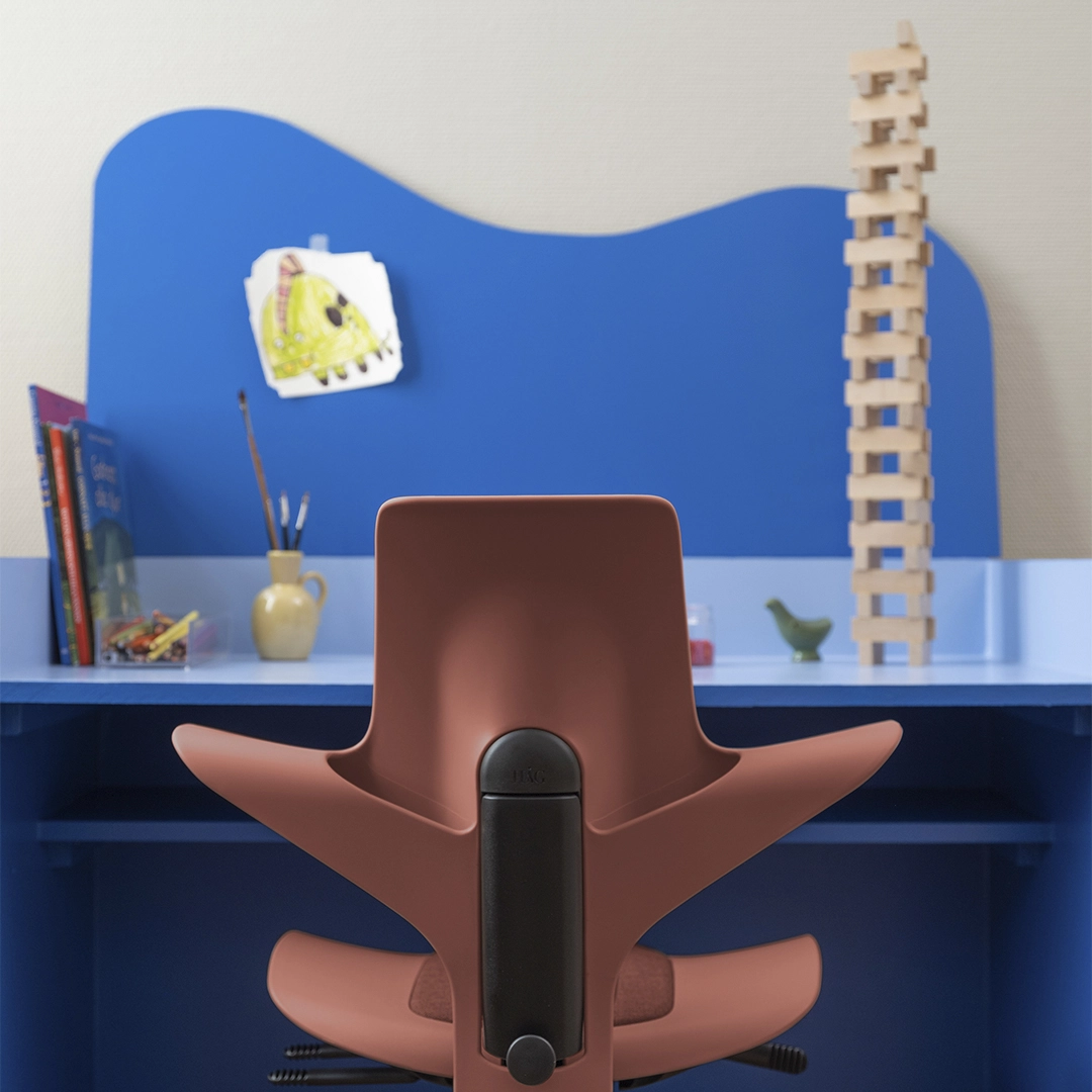 Blue desk with the pink little office chair in front. A Jenga tower and a painting placed on the table