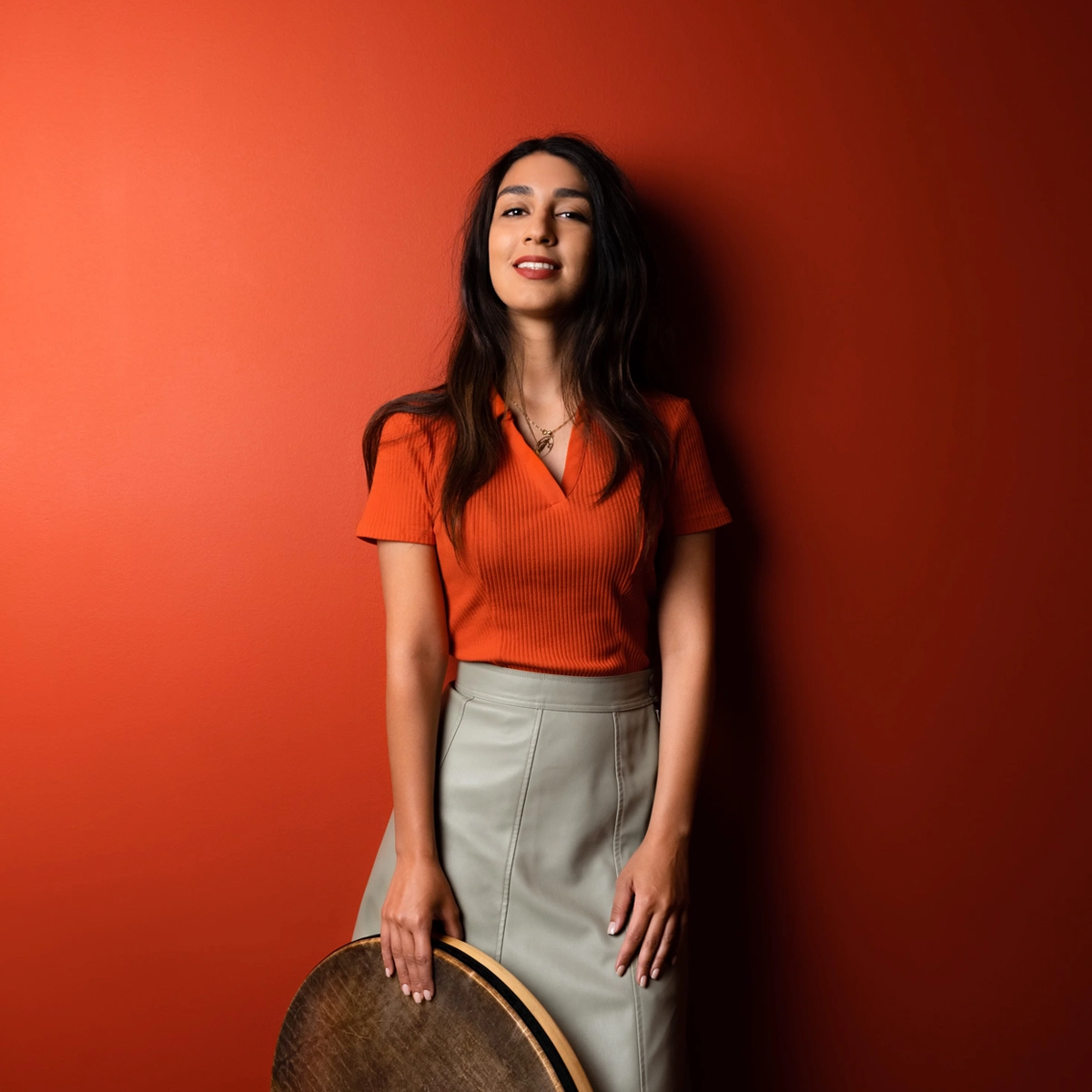 Woman in red shirt leaning against a red wall facing forward