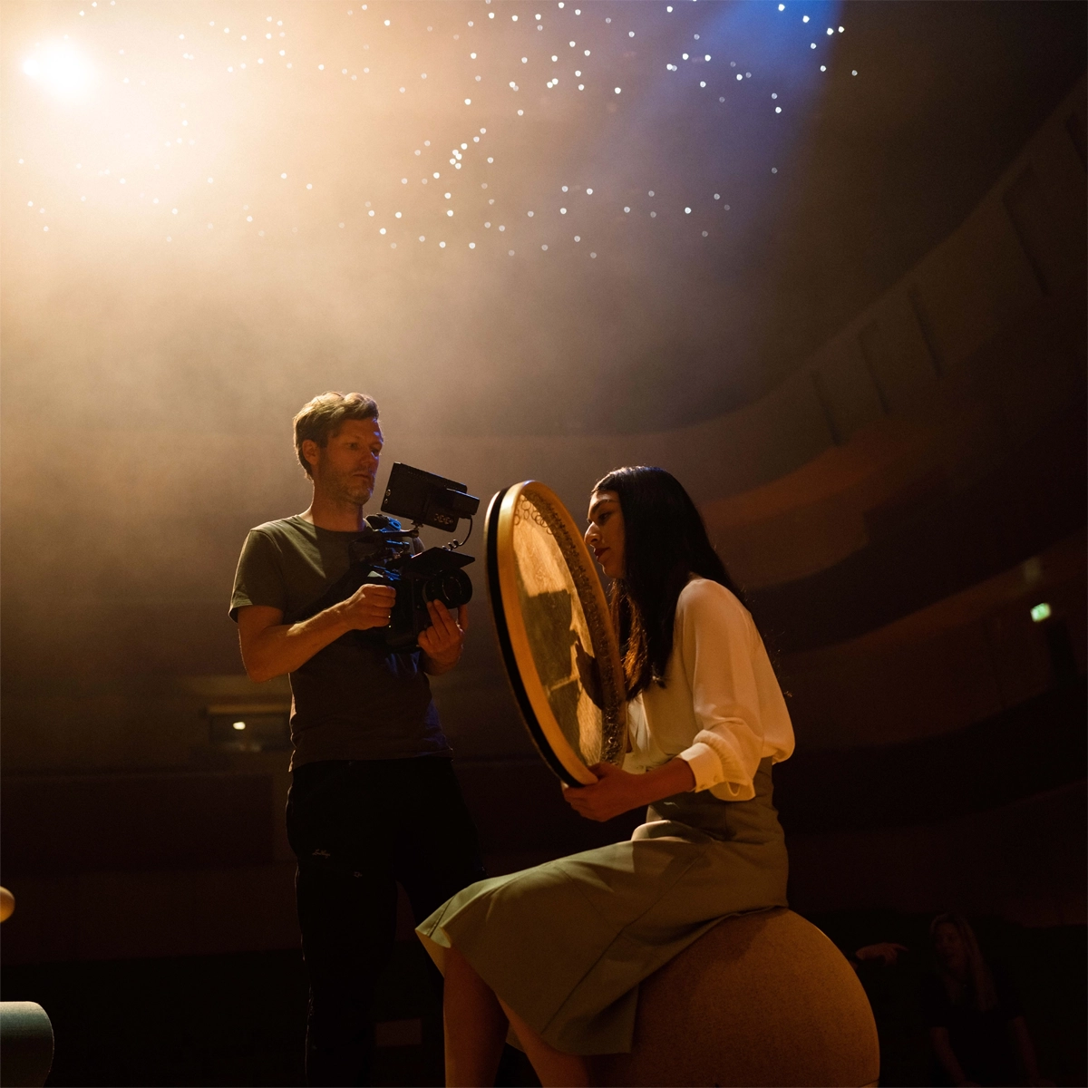 Man filming a woman on a stage sitting down