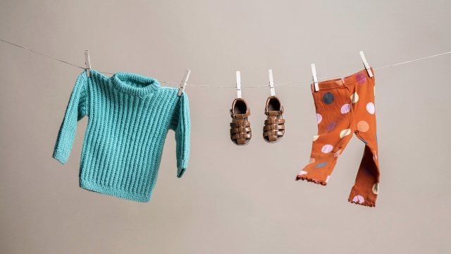 Three children's clothes a blue knitted cardigan, shoes and a pair of leggings on a clothesline attached with clothespins.