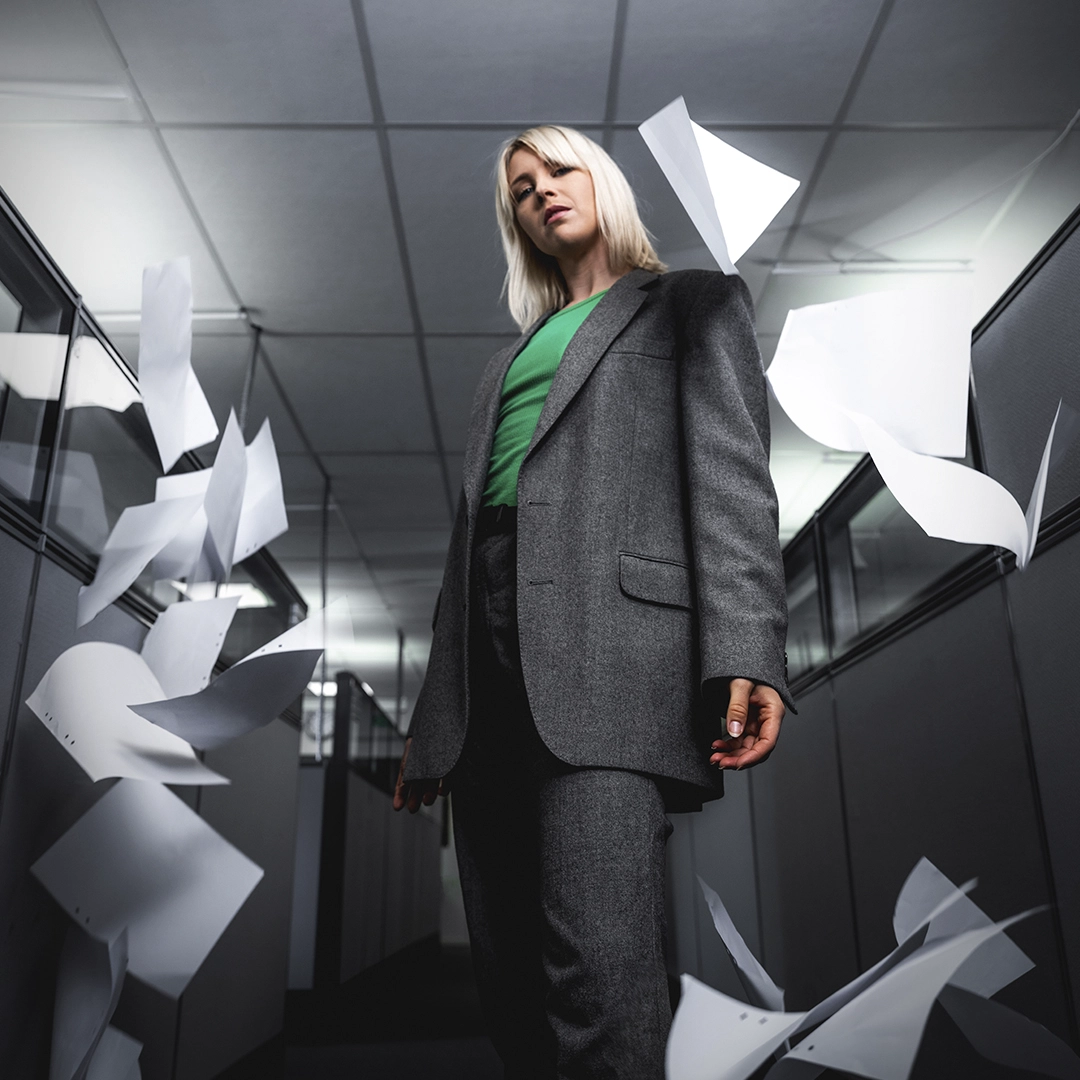 Woman in green t-shirt and suit in office, looking down into camera