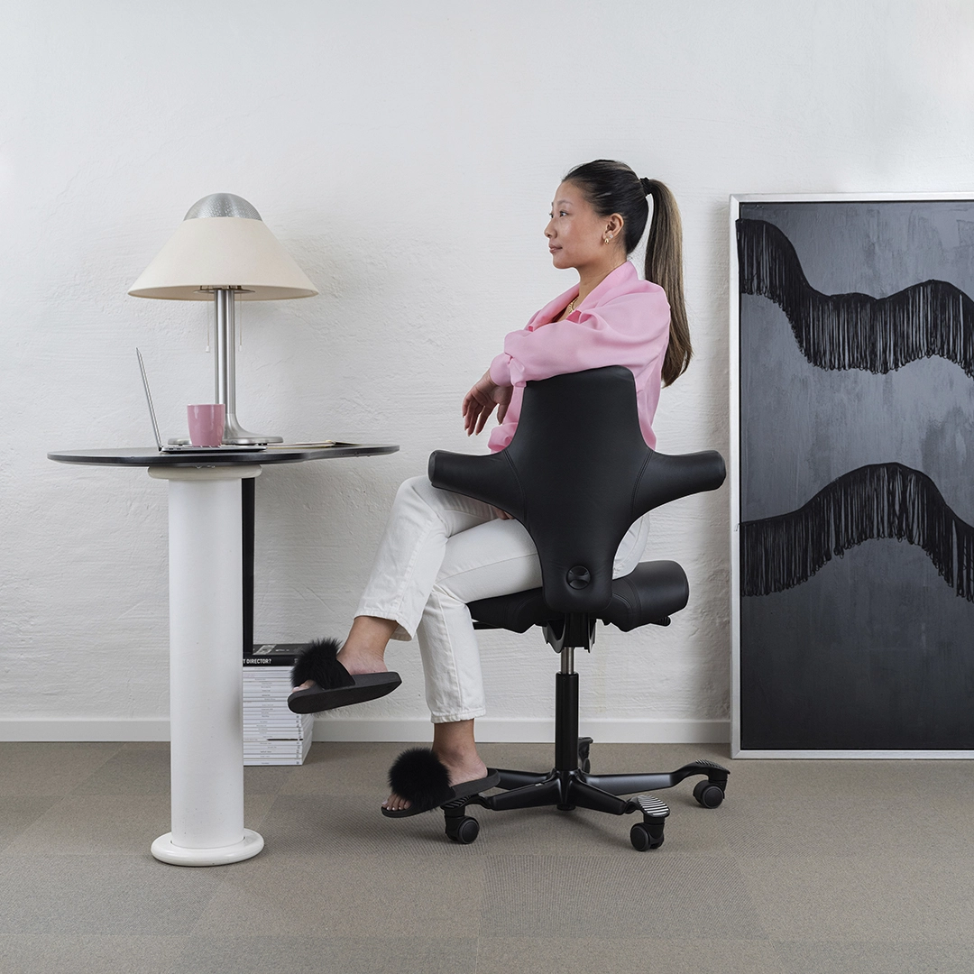a student room with office chair, painting and table. The woman sits on the black office chair-NyStudio