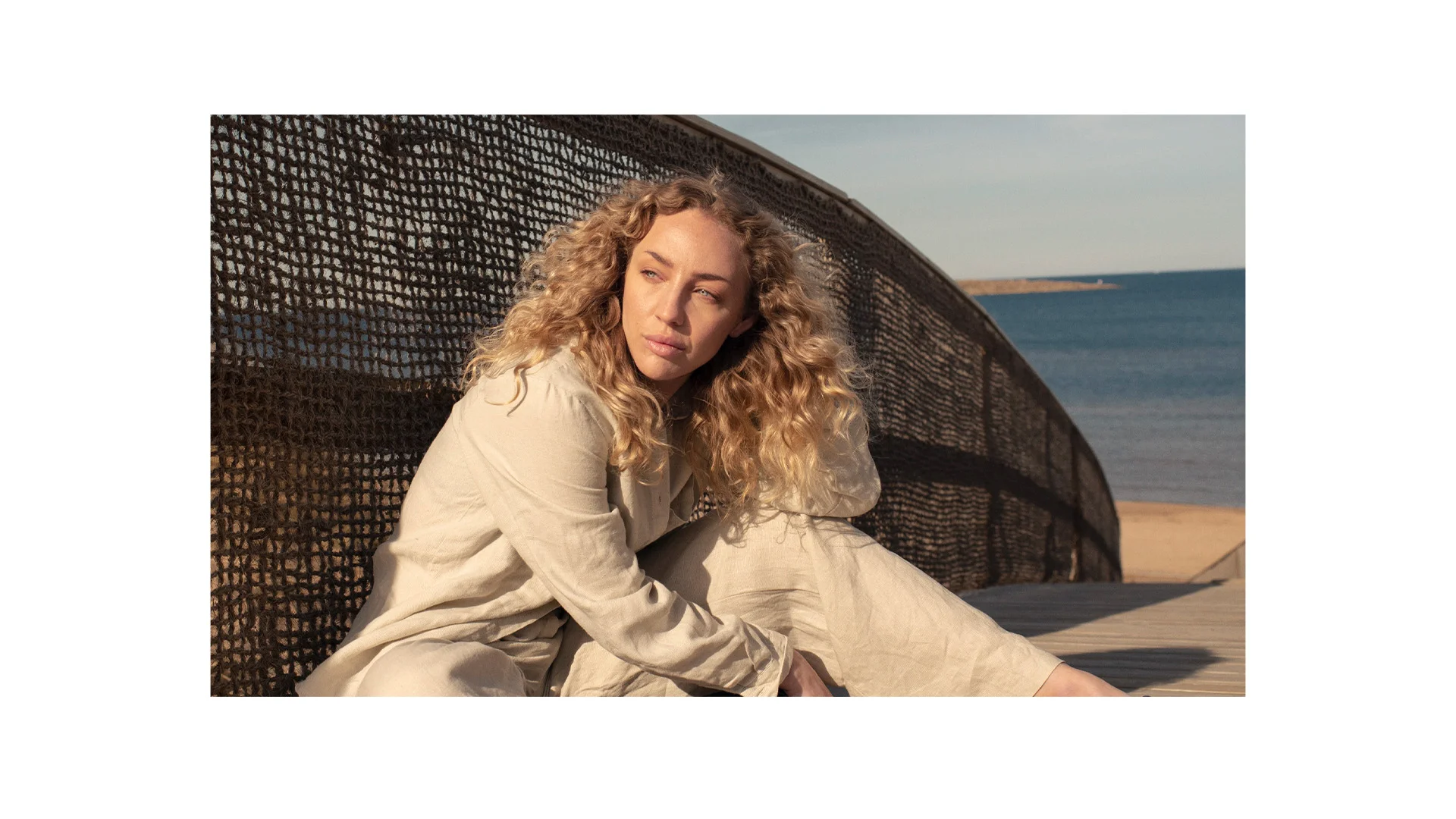 Kvinna som sitter på marken på en strand och kollar mot solnedgången