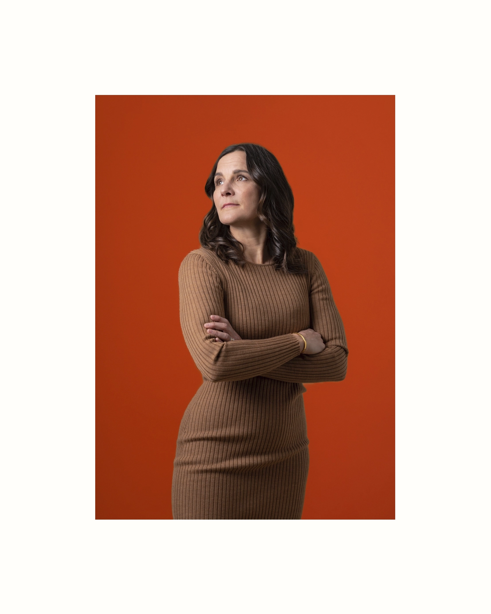 Woman standing with crossed arms with an orange background - Ny Studio