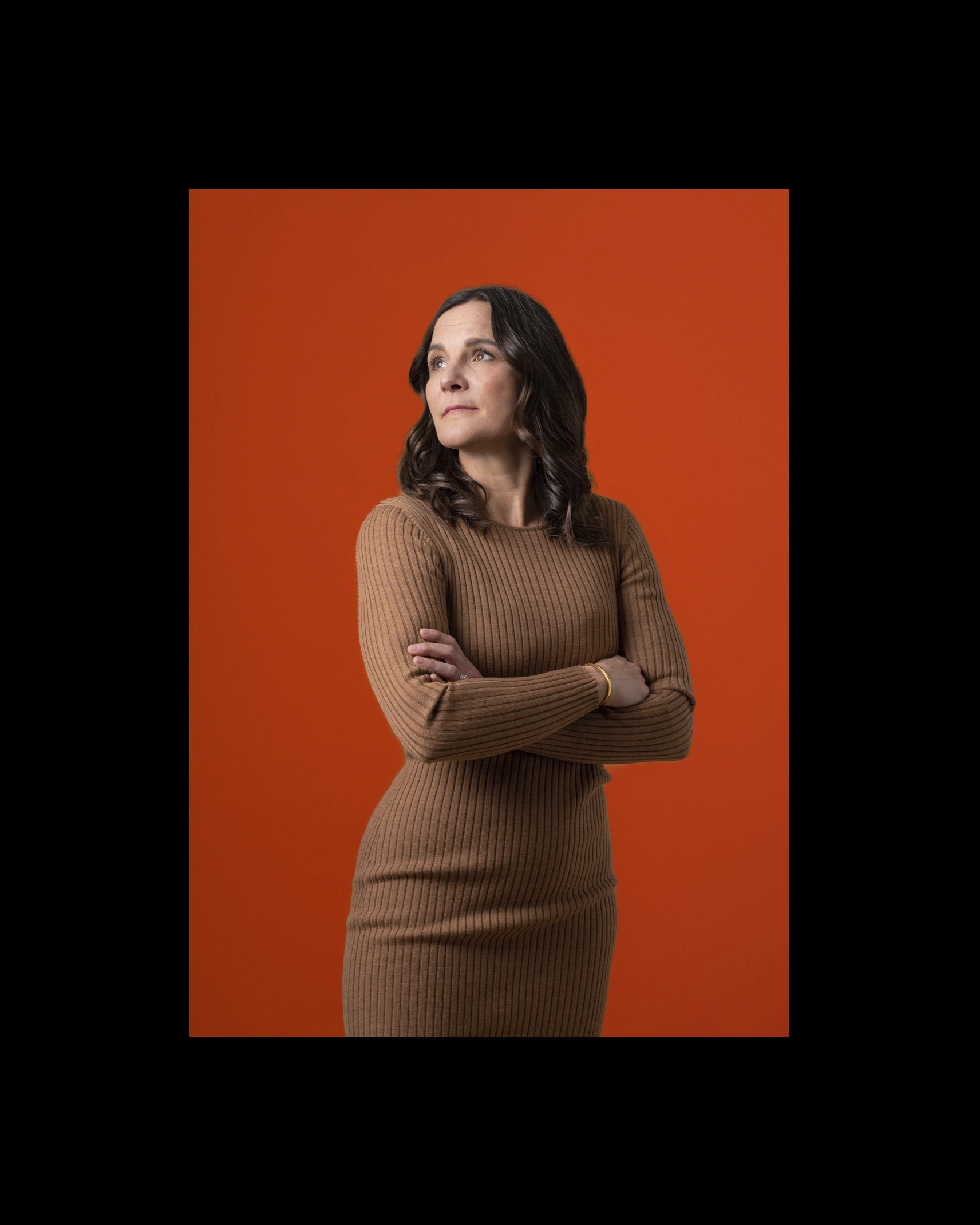 Woman standing with crossed arms with an orange background - Ny Studio